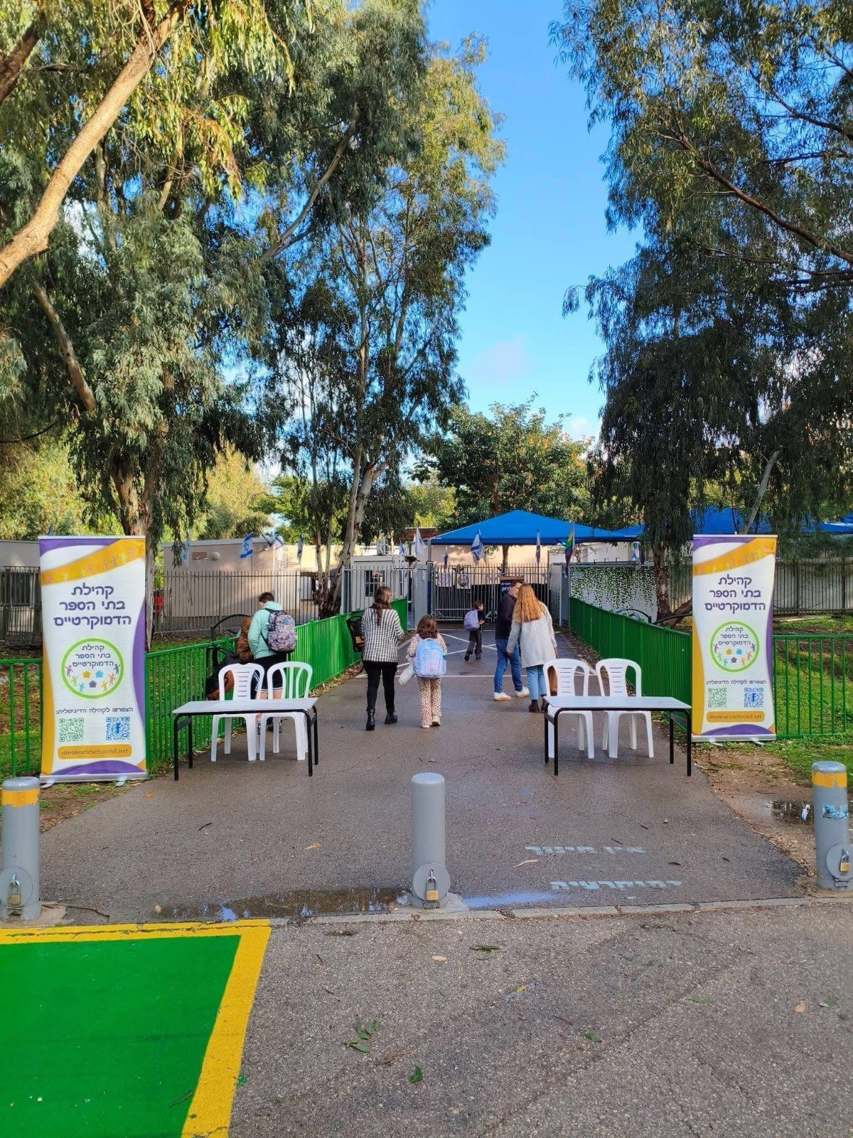 שביל כניסה בין עצים עם שני שלטים ושולחנות